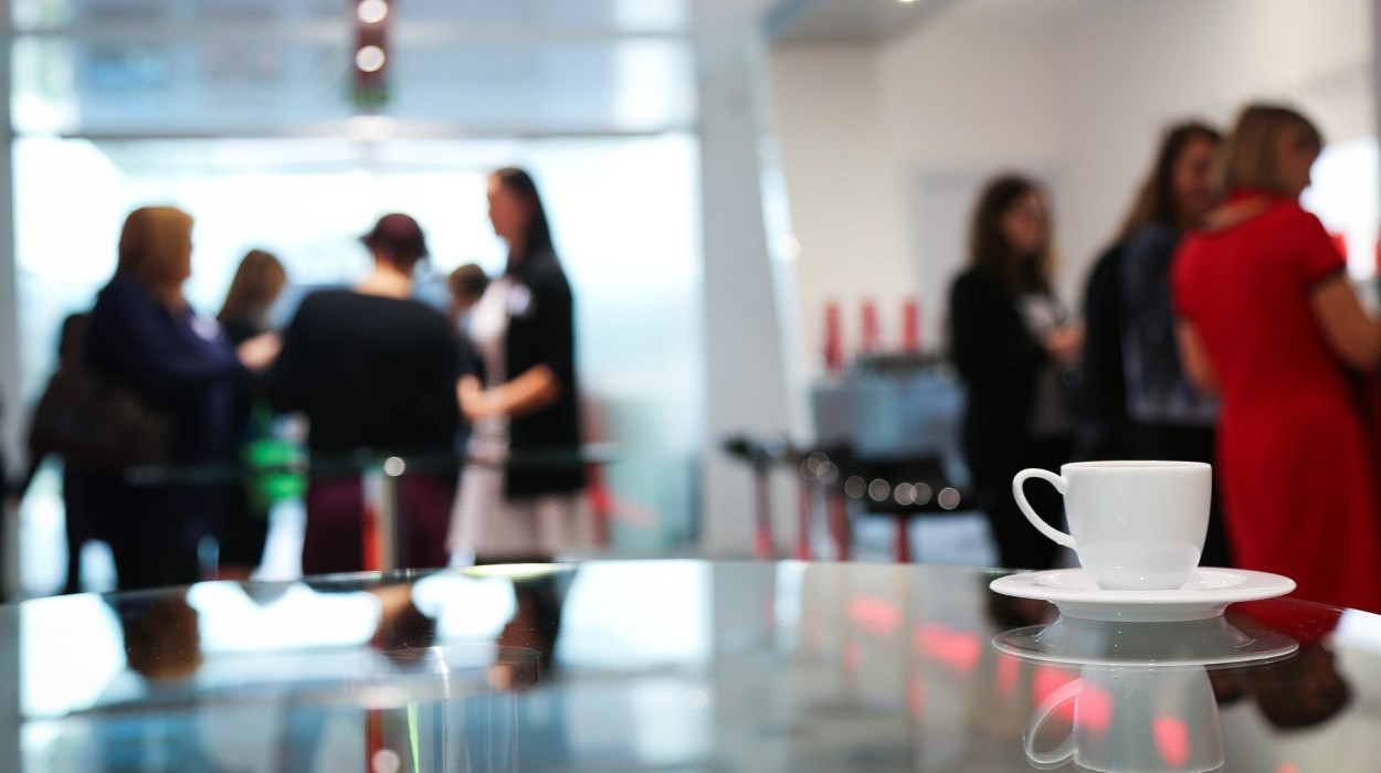 Coffee cup on a glass table with multiple people in business attire in the background