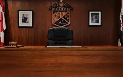 Large chair behind a wood desk with photos and the crest in the background. 