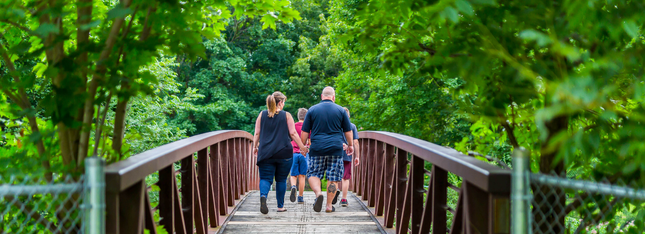 A family walking across a metal bridge surrounded by trees